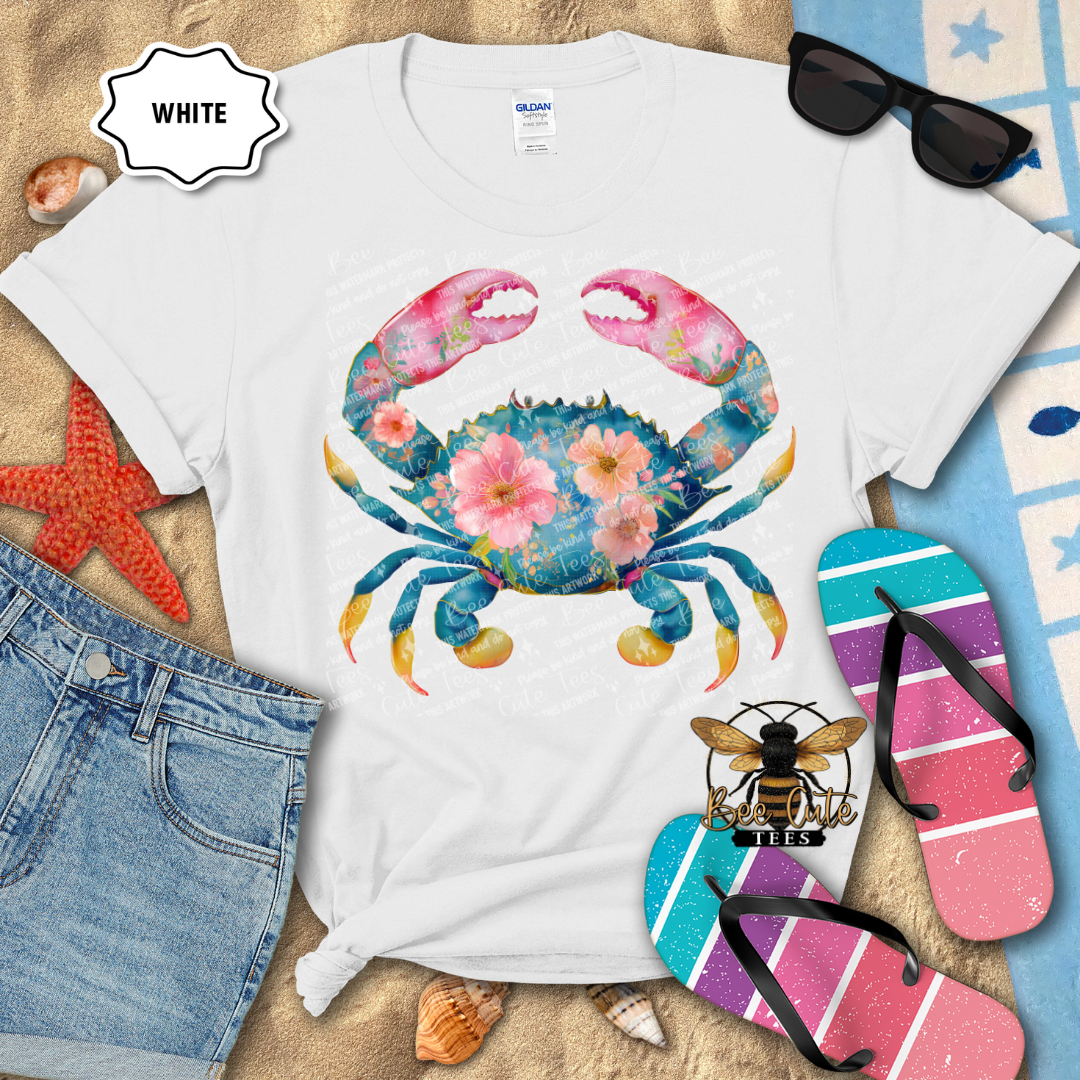 White t-shirt with a colorful crab design on a beach-themed background with flip-flops and sunglasses.