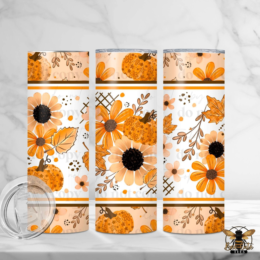 Three insulated tumblers with a fall floral pumpkin pattern, shown on a white marble surface with a clear lid in the foreground. The pattern features orange pumpkins, orange flowers, and brown leaves on a white background.