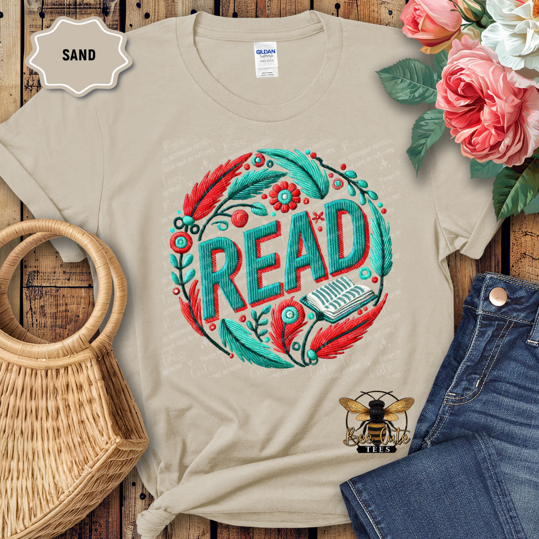 Beige t-shirt with 'READ' design on a wooden surface with flowers and jeans.