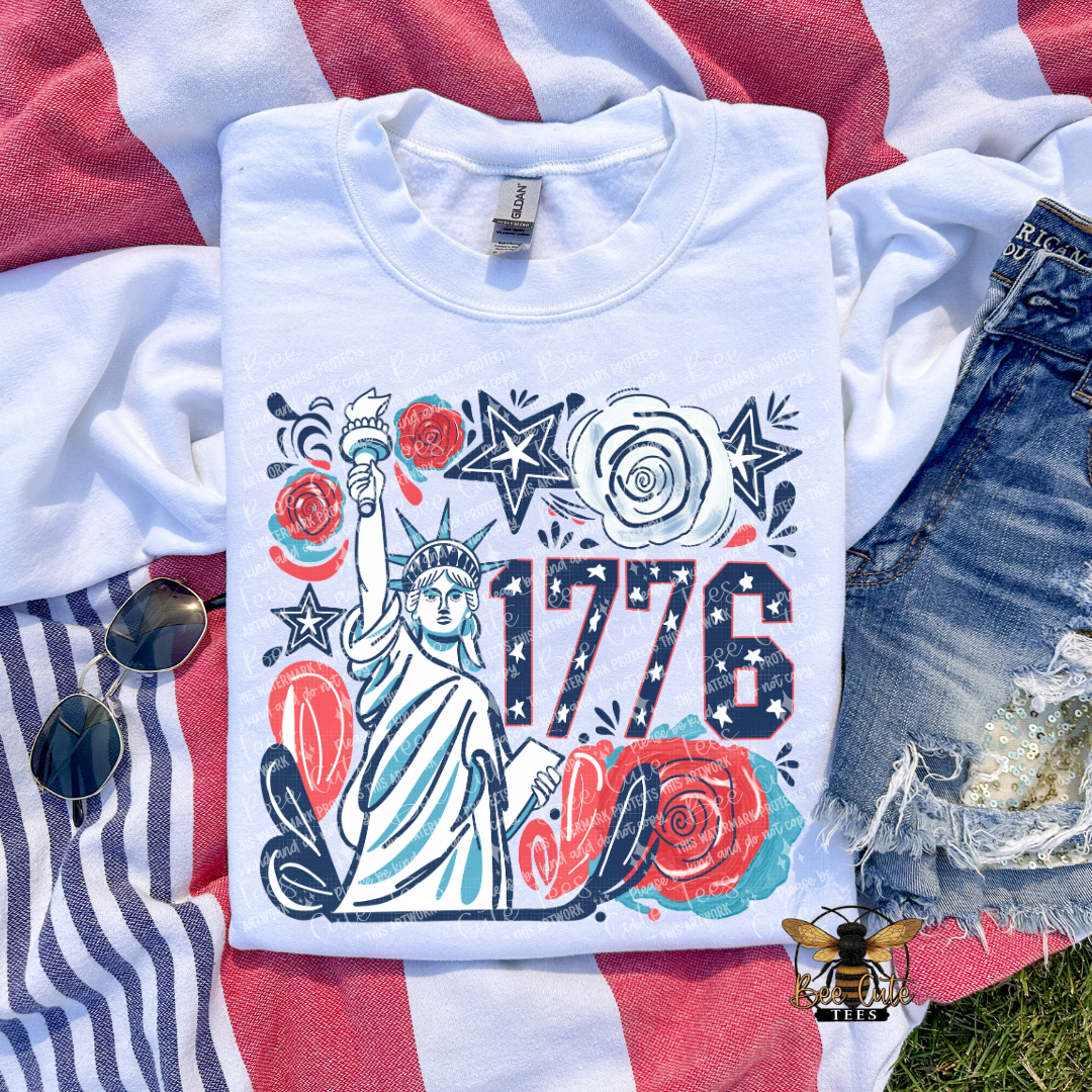 White t-shirt with 1776 design featuring the Statue of Liberty on a red, white, and blue striped fabric background.