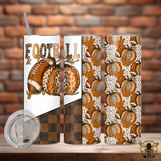 Three insulated tumblers with a fall football theme, featuring a graphic of footballs and the word 'FOOTBALL' on one tumbler, and repeating pumpkin and football patterns on the other two. A clear lid is shown in the foreground against a brick wall background.