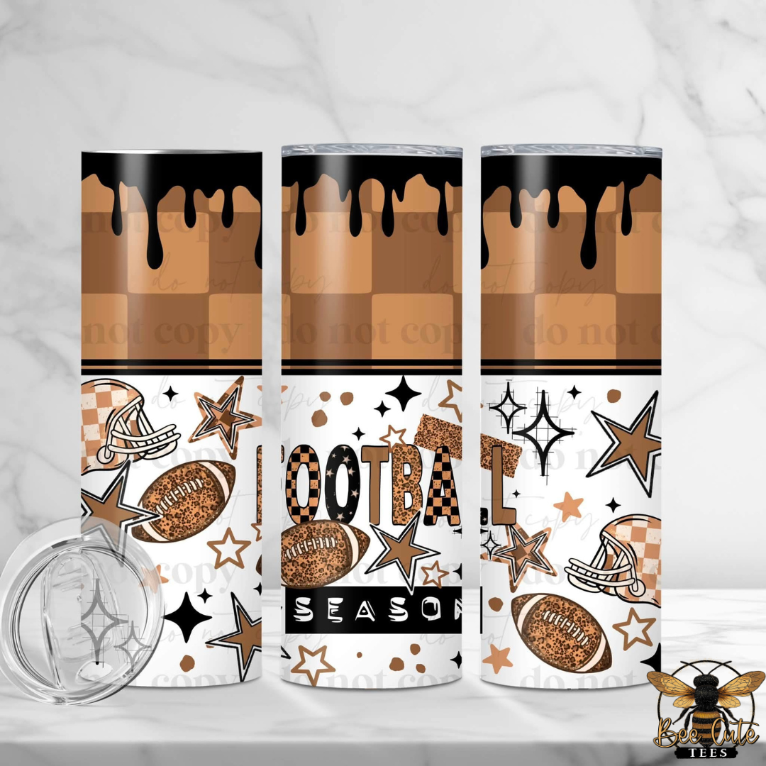 Three stainless steel skinny tumblers with a football-themed design, shown on a white marble surface with a clear lid in the foreground. The design features a brown and tan checkerboard pattern with black dripping paint at the top, white stars and stripes, footballs, helmets, and the words 'FOOTBALL SEASON'.