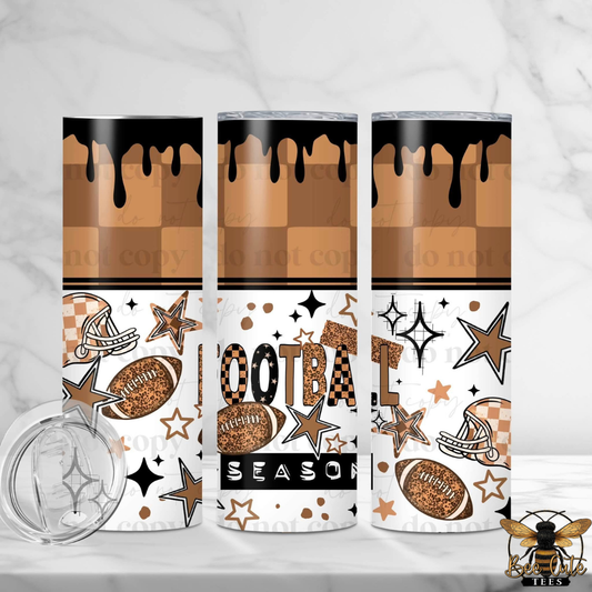 Three stainless steel skinny tumblers with a football-themed design, shown on a white marble surface with a clear lid in the foreground. The design features a brown and tan checkerboard pattern with black dripping paint at the top, white stars and stripes, footballs, helmets, and the words 'FOOTBALL SEASON'.