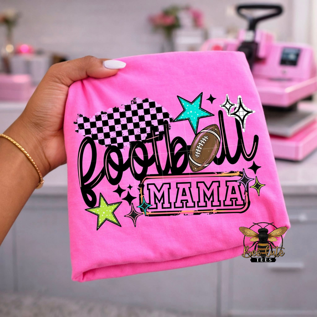Pink t-shirt with 'Football Mama' design held by a hand, with a blurred background.