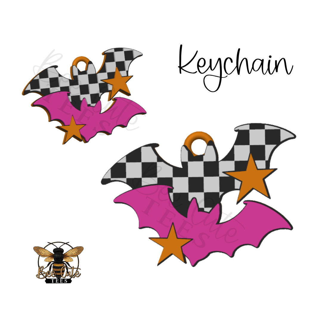 Two Halloween-themed bat keychain charms with a black and white checkered pattern, bright pink wings, and orange stars, shown on a white background with the word 'Keychain' and a small bee logo.