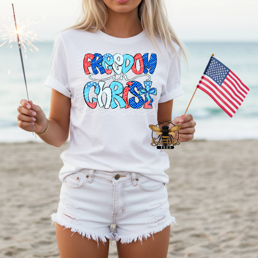 Person on a beach wearing a white t-shirt with 'Freedom Christ' text, holding an American flag and a sparkler.