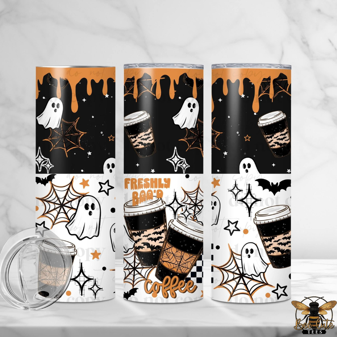 Three tall insulated tumblers with Halloween-themed wraps are shown on a light marble surface and background. The designs feature black and white sections with orange accents, including ghosts, spiderwebs, stars, coffee cups, and the words 'FRESHLY Boo'D coffee.