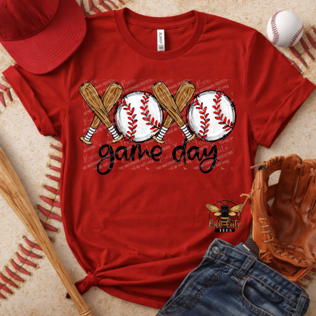 Red t-shirt with baseball graphics and 'game day' text, surrounded by baseball equipment on a textured surface.