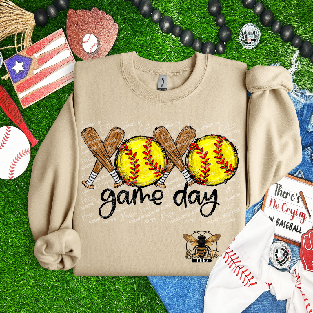 Beige sweatshirt with softball design and 'game day' text on a grass background with sports-themed accessories.