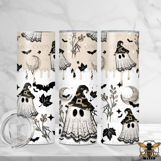 Three tall skinny tumblers with a Halloween-themed print featuring ghosts, witches, bats, and moons on a cream and white background, shown on a light marble surface with a clear lid in the foreground.