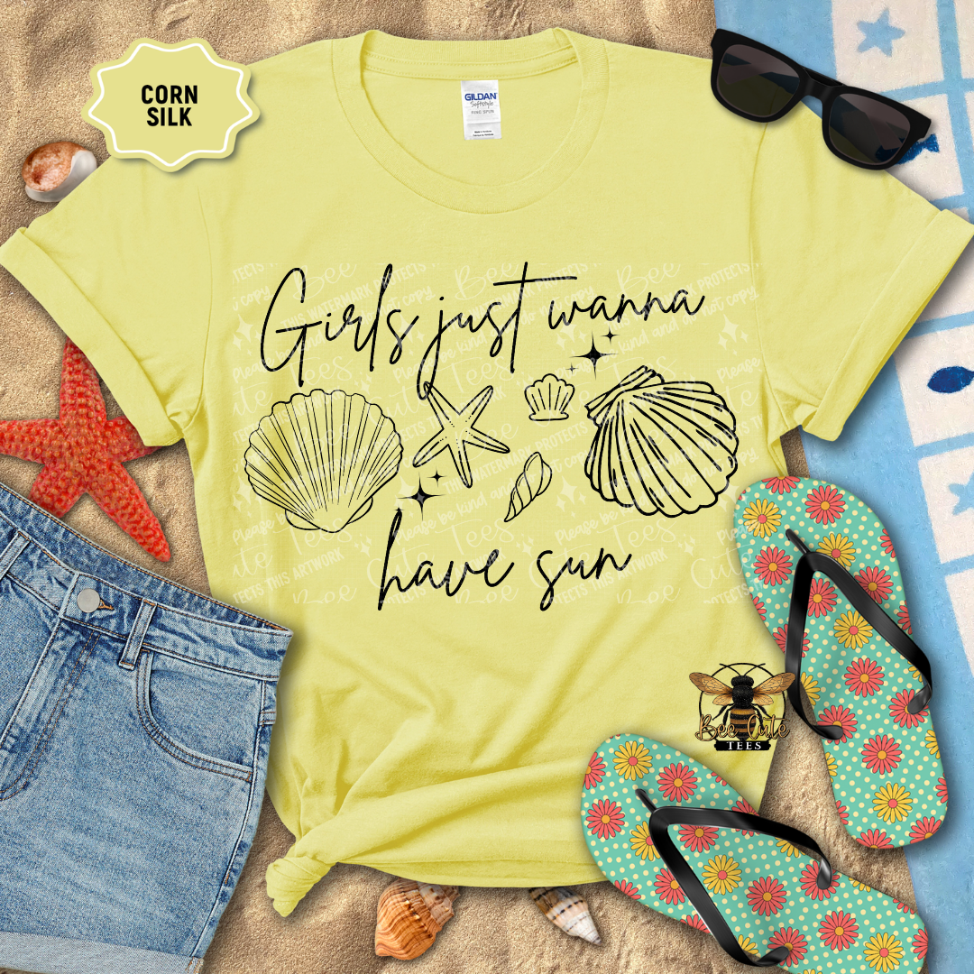 Yellow t-shirt with 'Girls just wanna have sun' text and beach-themed graphics on a sandy background with flip-flops and sunglasses.