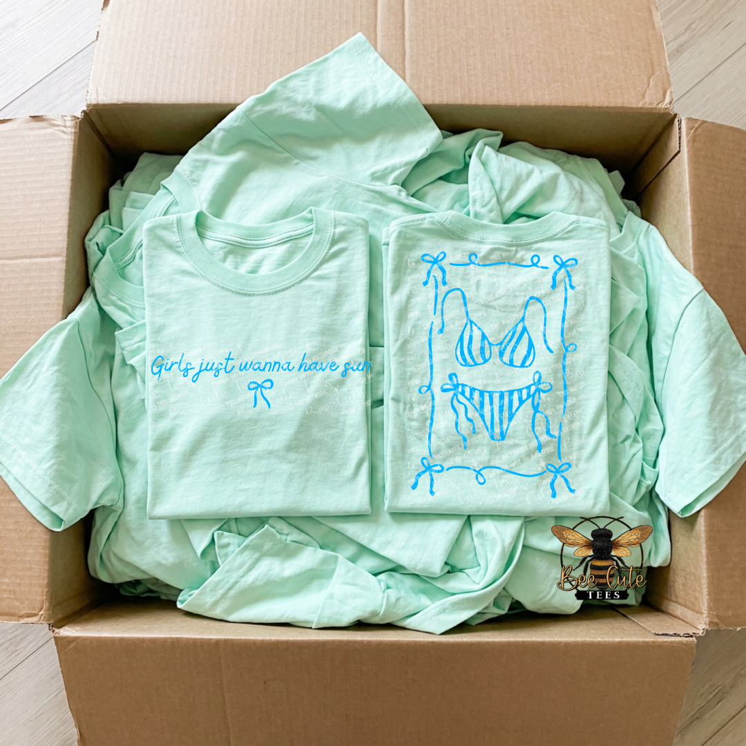 Box filled with light green t-shirts featuring blue graphics and text.
