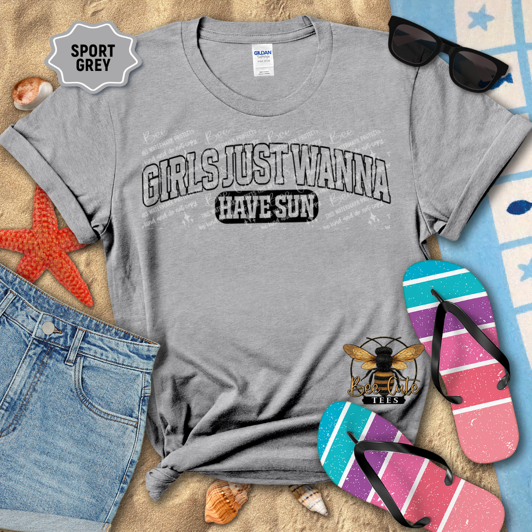 Gray t-shirt with 'Girls Just Wanna Have Sun' text, sunglasses, flip-flops, and beach items on a sandy background.