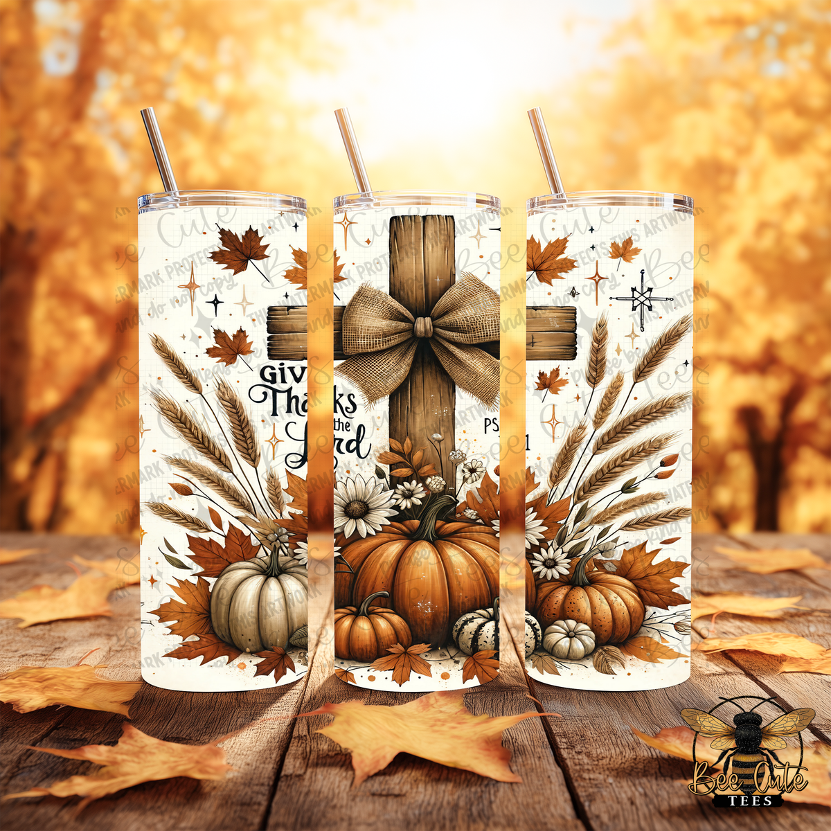 Three clear insulated tumblers with metal straws are shown on a wooden surface against a warm autumn tree background. The tumblers have a fall harvest print with pumpkins, wheat, leaves, flowers, and decorative text.