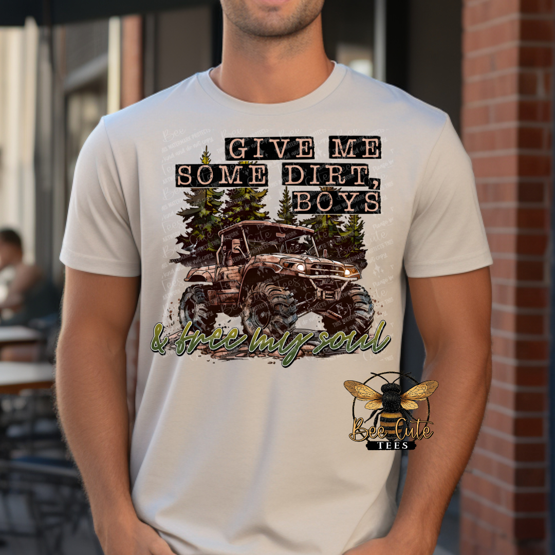 Man wearing a light beige graphic tee featuring a lifted off-road mud truck surrounded by pine trees with the phrase “Give Me Some Dirt, Boys” in rustic outdoor-style lettering.
