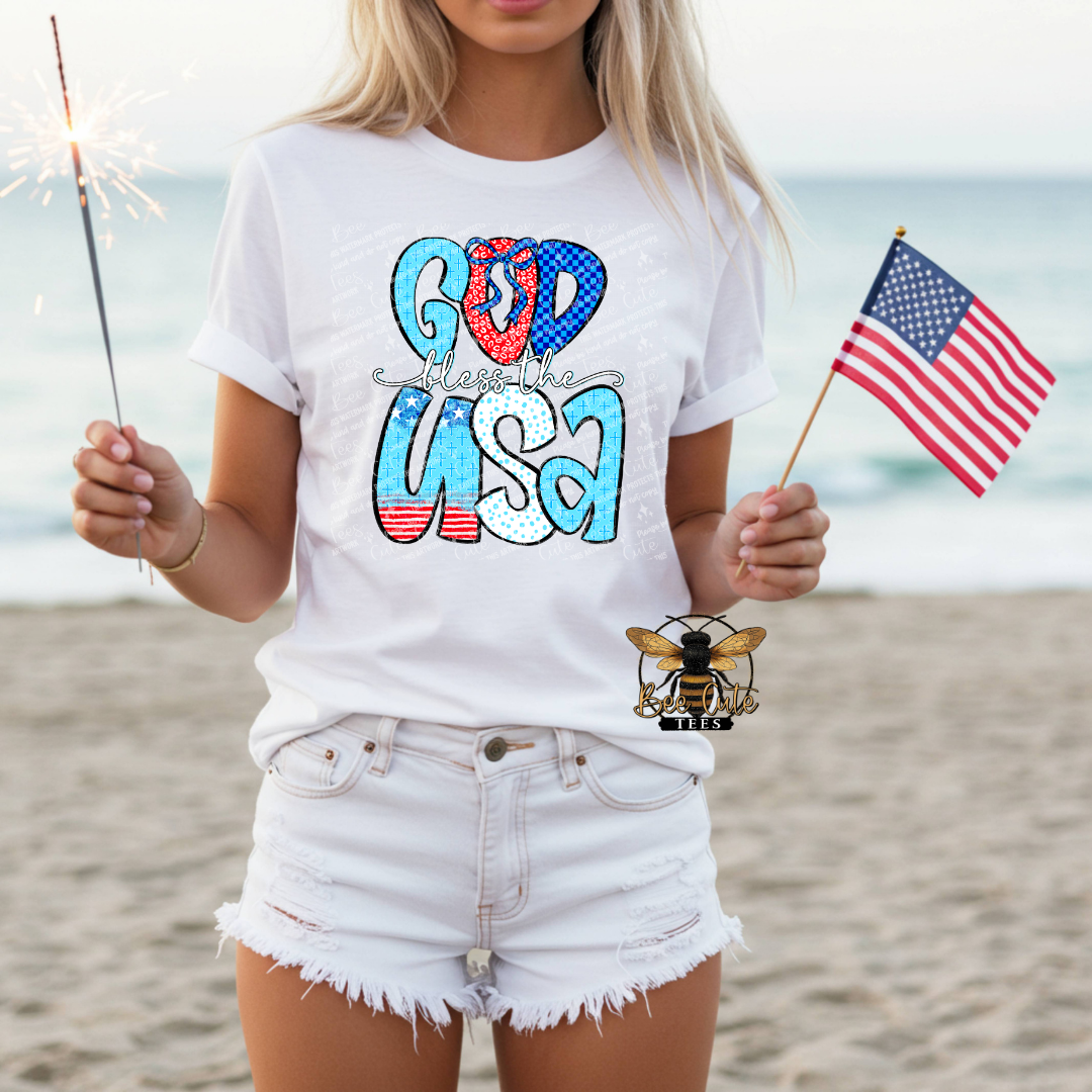 Person wearing a white t-shirt with 'God Bless the USA' design on a beach.
