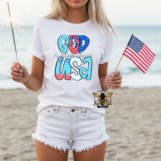 Person wearing a white t-shirt with 'God Bless the USA' design on a beach.