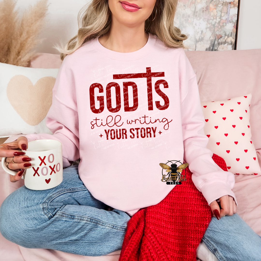Person wearing a pink sweatshirt with motivational text, holding a mug, sitting on a couch with decorative pillows.