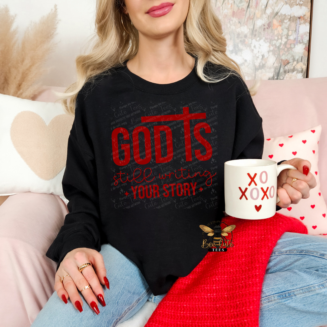 Person wearing a black sweatshirt with red text, holding a mug with heart designs, sitting on a couch.