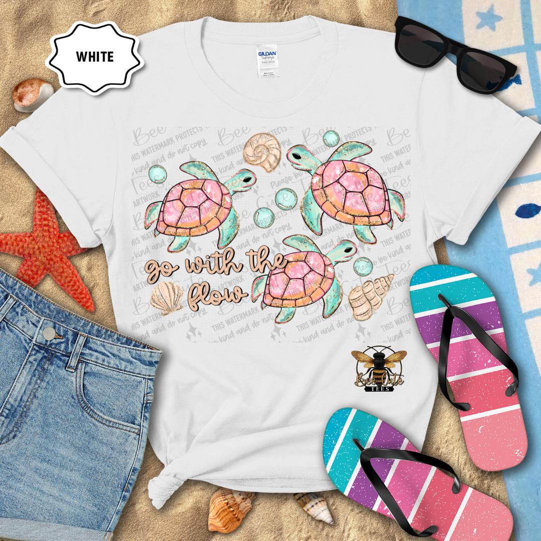 White t-shirt with turtle design and 'go with the flow' text, surrounded by beach accessories.