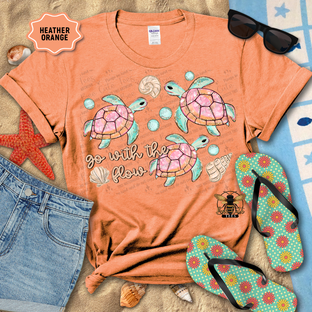 Orange t-shirt with turtle design and 'go with the flow' text, surrounded by beach accessories.