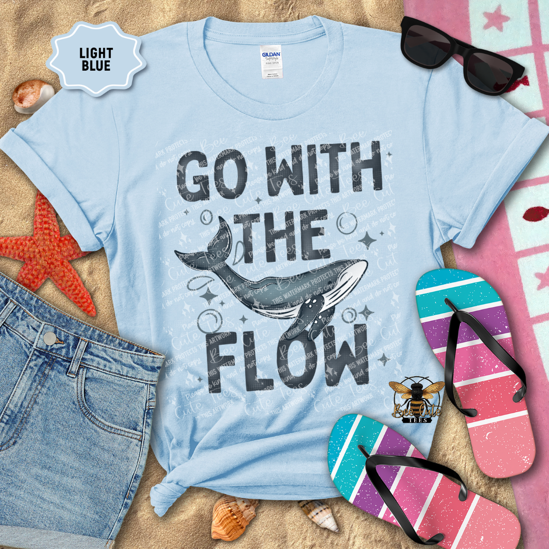 Light blue t-shirt with whale graphic and 'Go With The Flow' text on a beach-themed background.