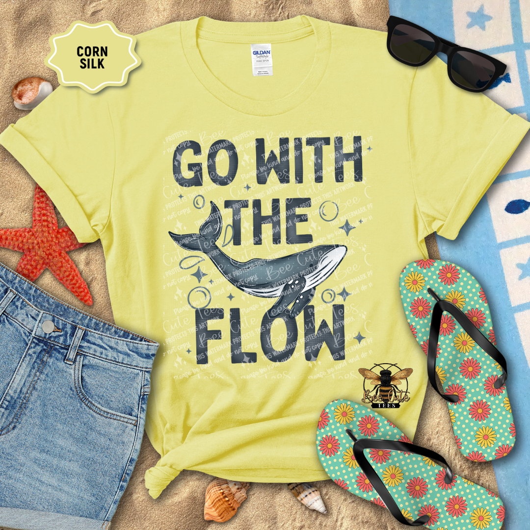 Yellow t-shirt with 'Go with the Flow' design on a beach setting with sunglasses, flip-flops, and denim shorts.