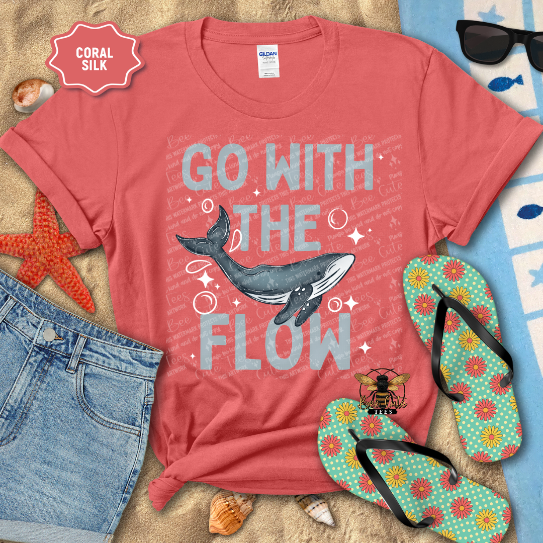 Coral t-shirt with whale graphic and 'Go with the Flow' text, surrounded by beach accessories.
