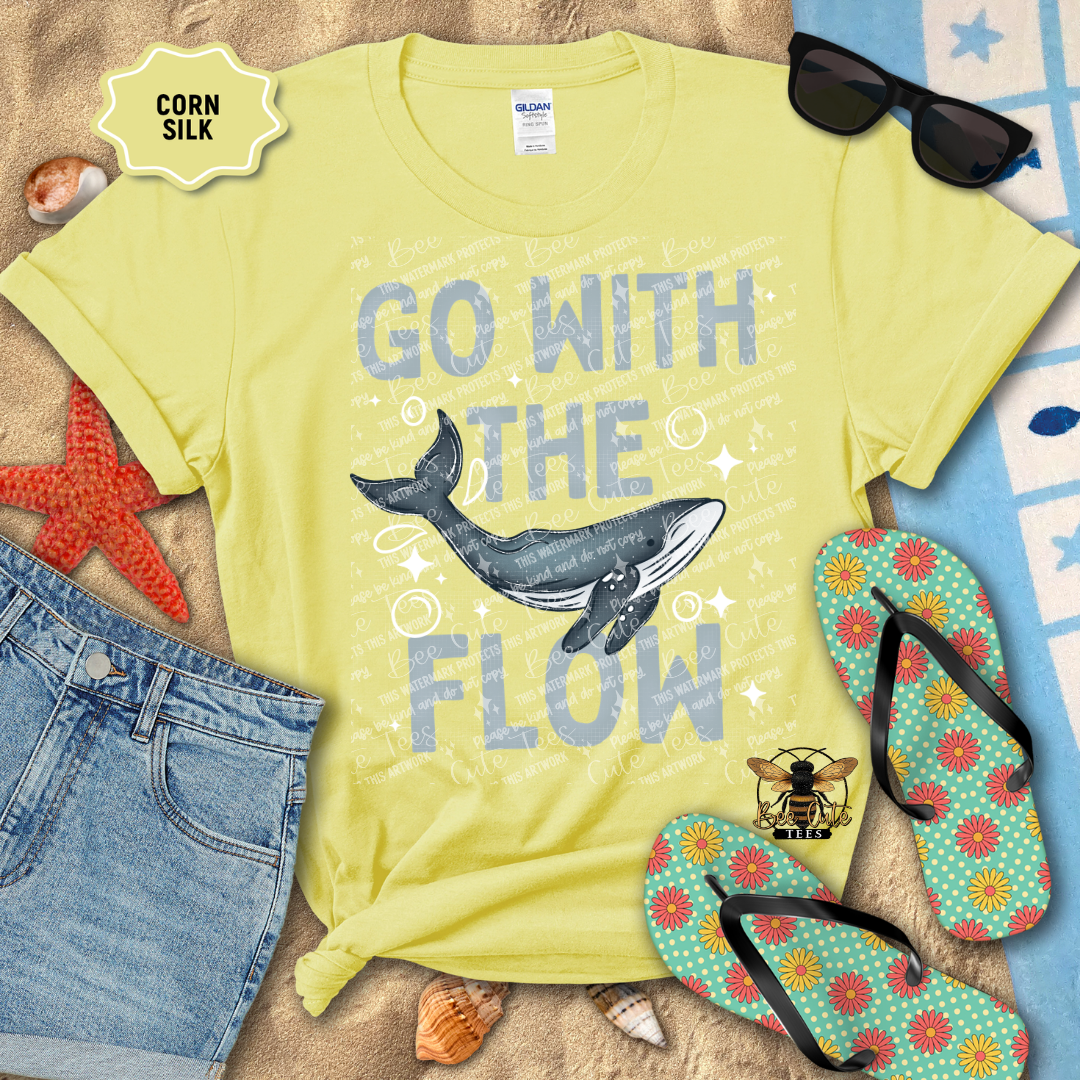 Yellow t-shirt with whale graphic and 'Go with the Flow' text, surrounded by beach accessories.