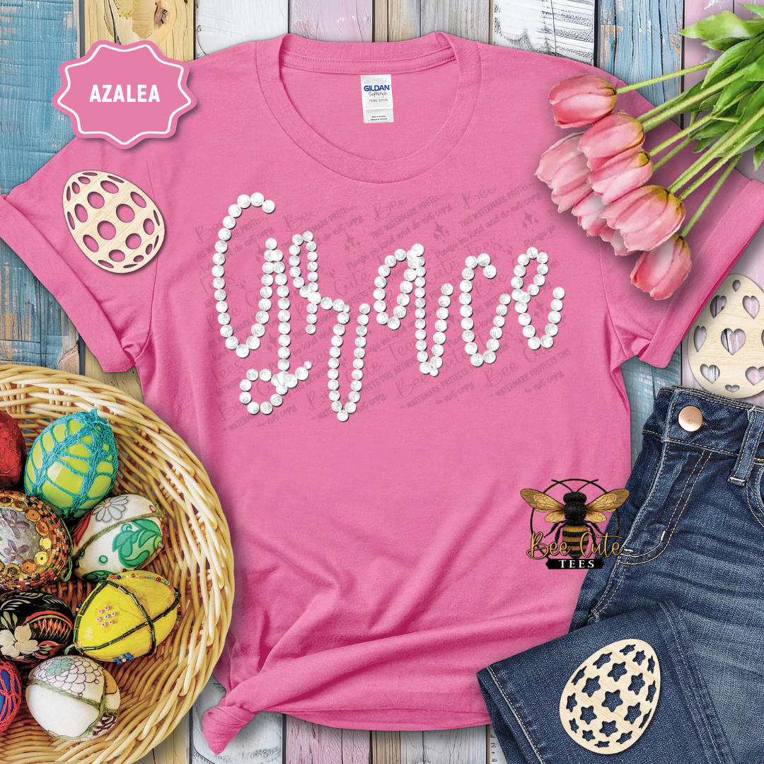 Pink t-shirt with 'Grace' design, surrounded by Easter decorations on a wooden surface.