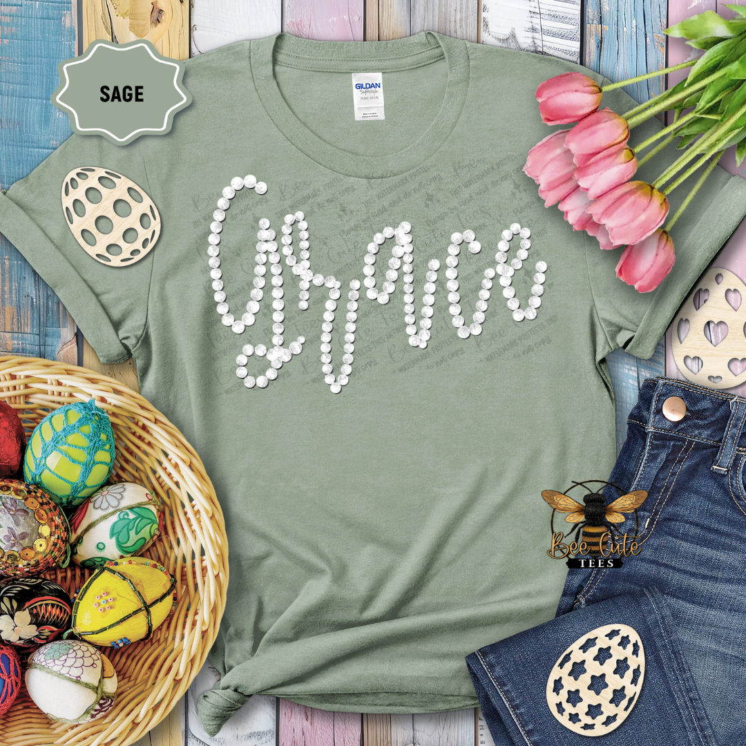 Green t-shirt with 'Gracie' in pearls, surrounded by Easter decorations on a wooden surface.