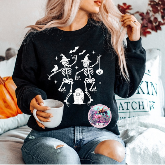 A person sitting on a couch wearing a black short sleeve t-shirt with a white graphic of skeletons and the text 'R.I.P
