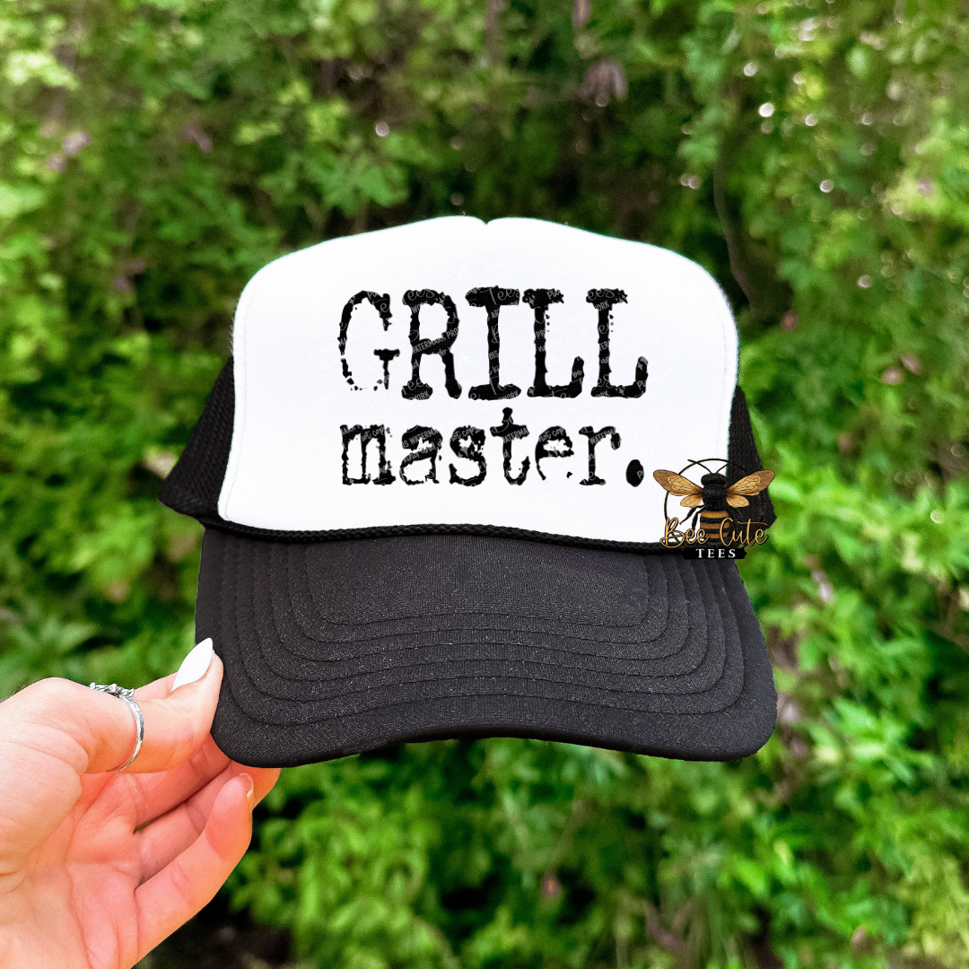 Black and white cap with 'GRILL master.' text held against a green leafy background