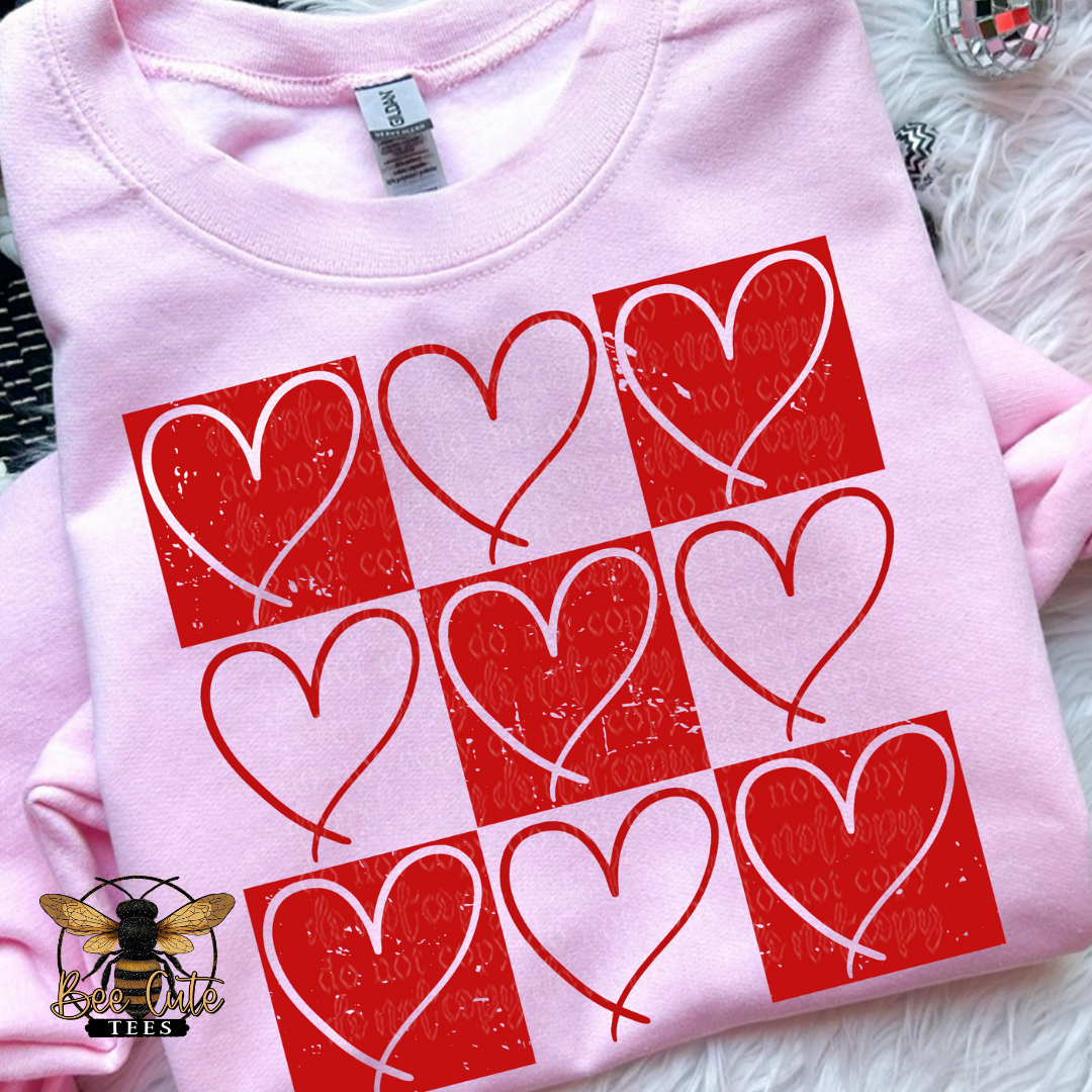 A pink short-sleeved t-shirt with a grid pattern of red heart shapes, each with a visible vein, on a white background. The t-shirt is displayed on a fluffy surface with a bee logo in the corner.