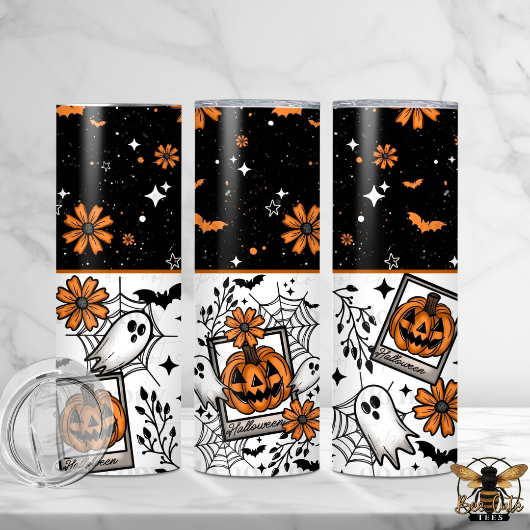 Three Halloween-themed tumblers with a matching clear lid are displayed on a light marble surface. The tumblers feature a split design: the top half is black with orange flowers, bats, and white stars, while the bottom half is white with orange flowers, bats, spiderwebs, and ghosts.