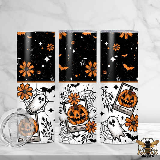 Three Halloween-themed tumblers with a matching clear lid are displayed on a light marble surface. The tumblers feature a split design: the top half is black with orange flowers, bats, and white stars, while the bottom half is white with orange flowers, bats, spiderwebs, and ghosts.