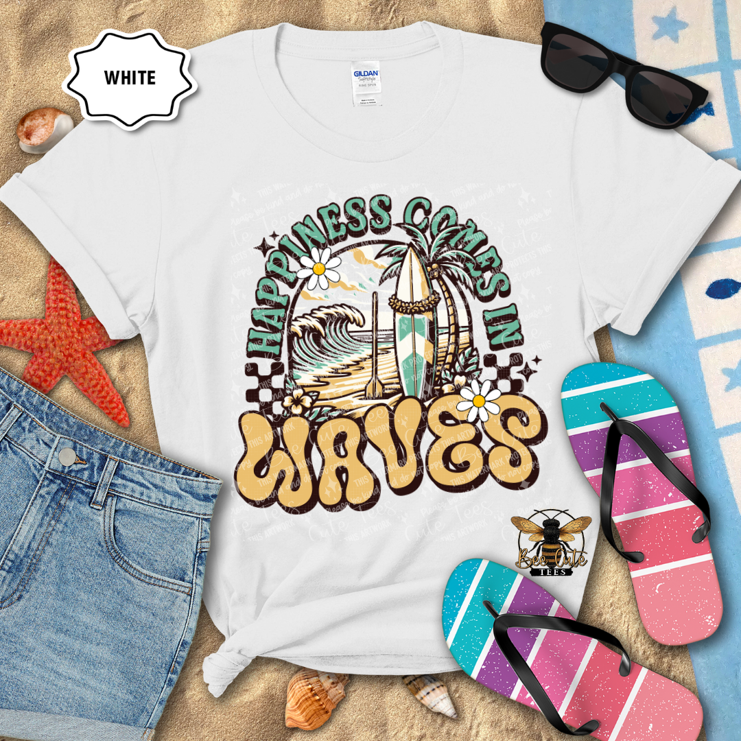 White t-shirt with 'Happiness Comes in Waves' design on a beach-themed background with flip-flops and sunglasses.