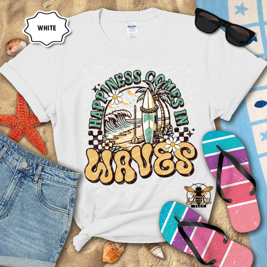 White t-shirt with 'Happiness Comes in Waves' design on a beach-themed background with flip-flops and sunglasses.