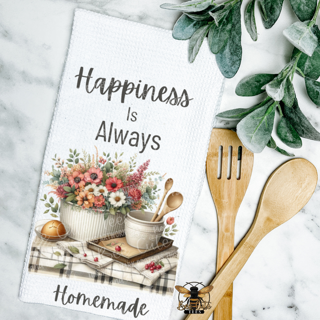 Kitchen towel with floral design and text 'Happiness is Always Homemade' on a marble surface with wooden utensils.
