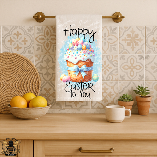 Kitchen towel with Easter design hanging on a towel rack, featuring a cupcake and text.