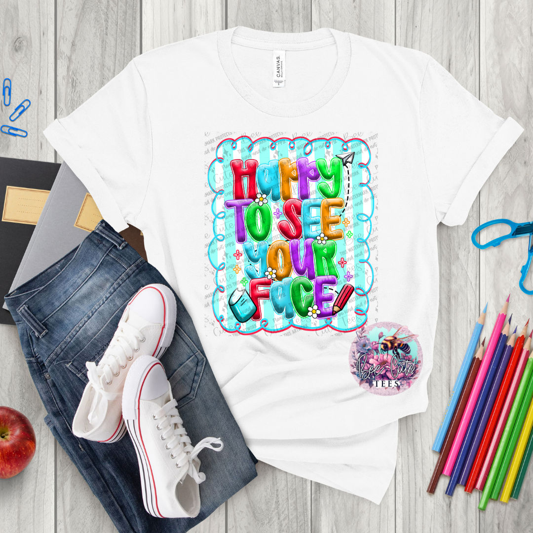 White t-shirt with colorful text design on a wooden surface with jeans, shoes, and stationery items.