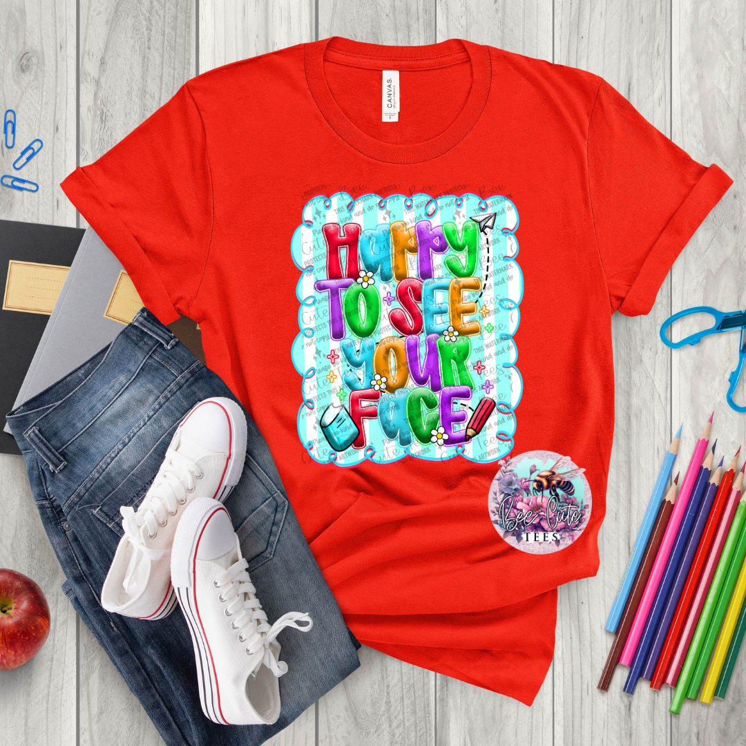 Red t-shirt with colorful graphic design on a wooden surface with jeans, sneakers, and stationery items.