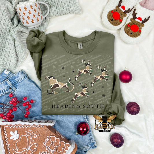 Green sweatshirt with illustrations and text, surrounded by Christmas decor on a white surface.