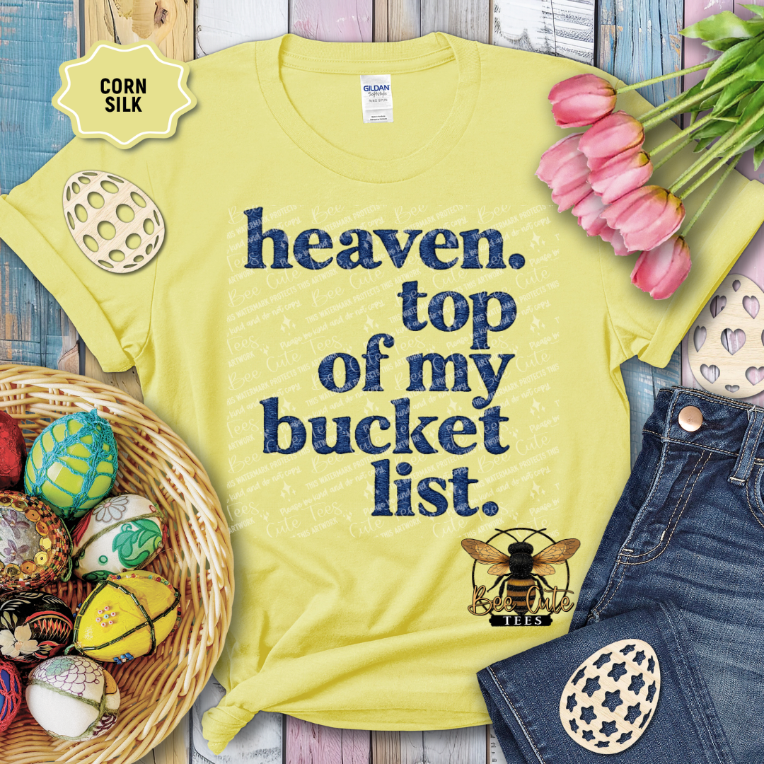 Yellow t-shirt with 'heaven. top of my bucket list.' text and bee graphic, surrounded by Easter decorations.