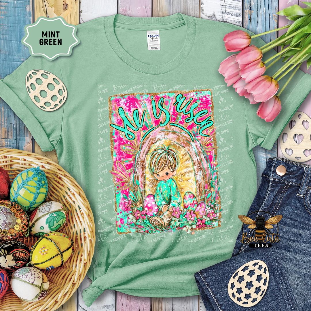 Mint green t-shirt with Easter-themed design featuring a child and eggs, surrounded by Easter decorations.