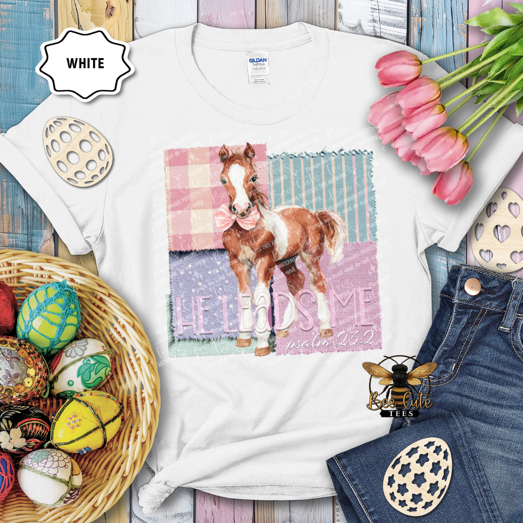 White t-shirt with a horse graphic and text, surrounded by Easter decorations on a wooden surface.