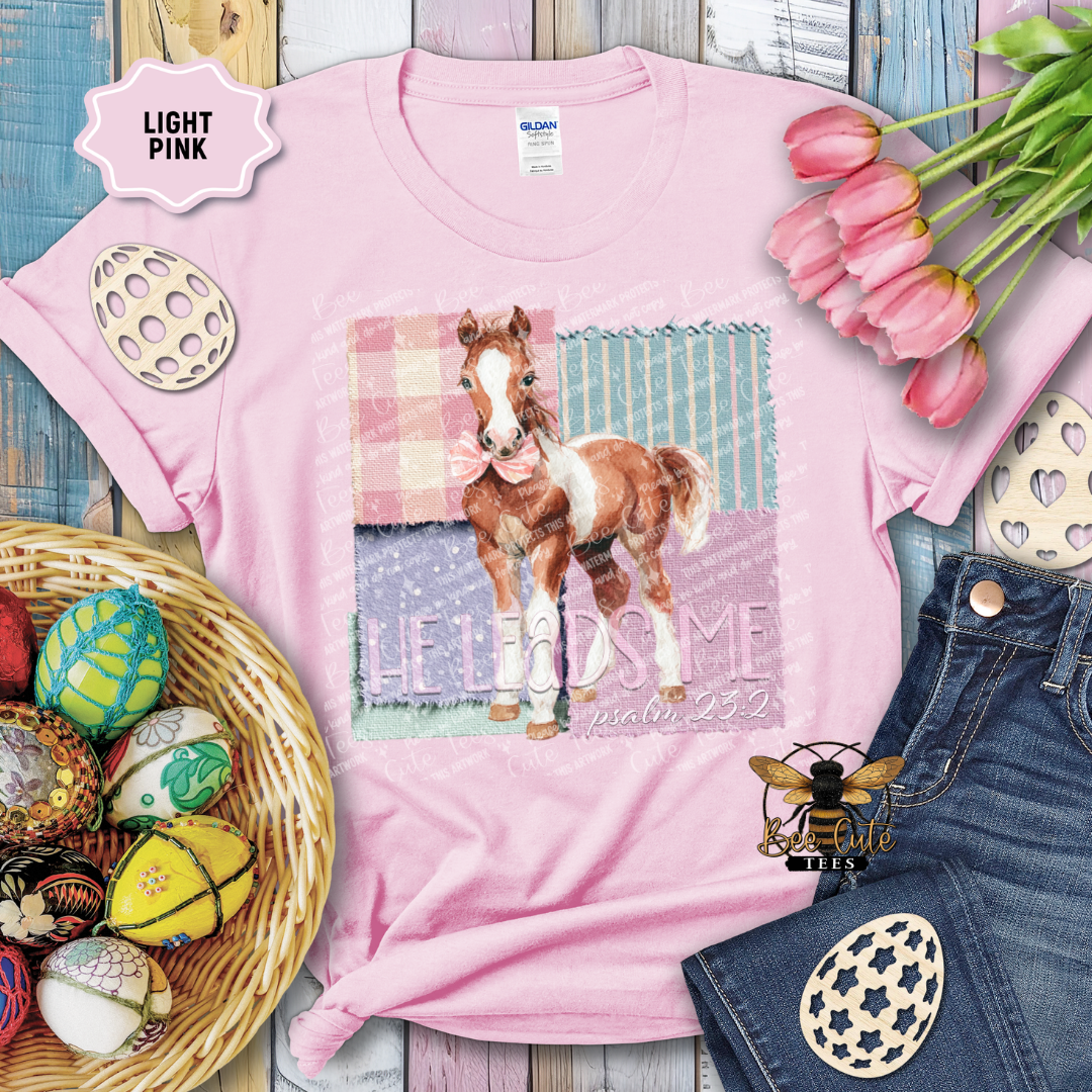 Pink t-shirt with a horse graphic and text, surrounded by Easter decorations on a wooden surface.