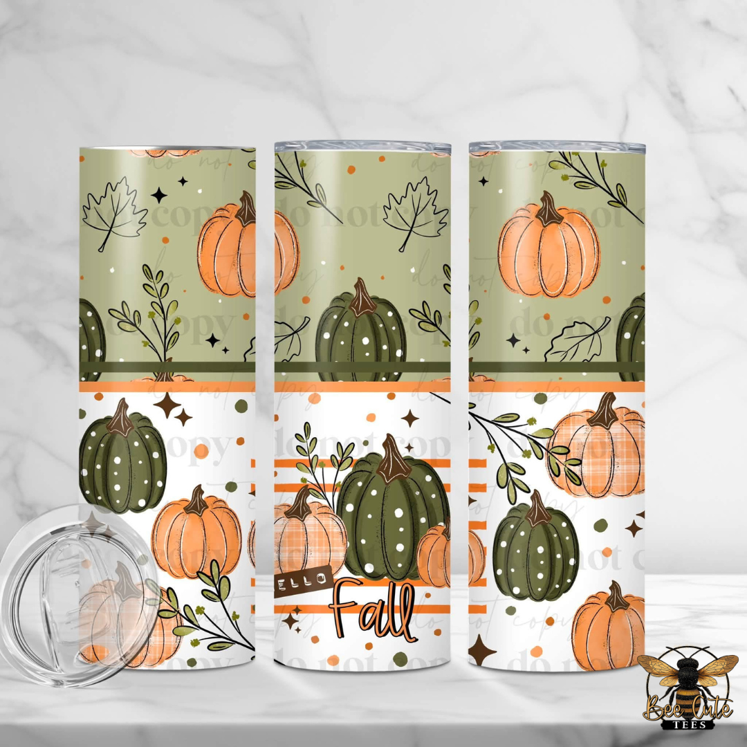 Three slim tumblers with a fall pumpkin pattern are displayed on a white marble surface, alongside a clear plastic lid. The tumblers feature a repeating design of orange pumpkins, green pumpkins, leaves, and stars on a sage green and white background with orange stripes.