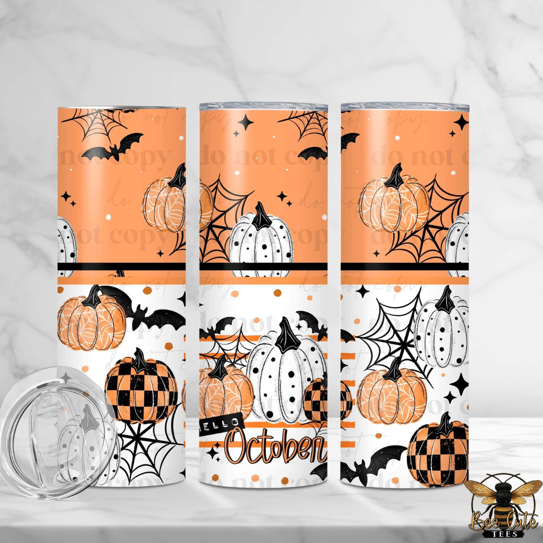 Three tall insulated tumblers with Halloween-themed prints are displayed on a light marble surface. The designs feature orange pumpkins, black spiderwebs, bats, stars, and the word 'October' in script.