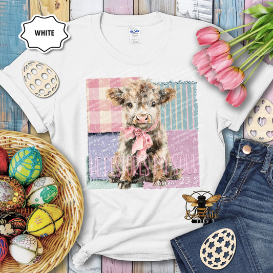 White t-shirt with a cow graphic and text, surrounded by Easter decorations on a wooden surface.